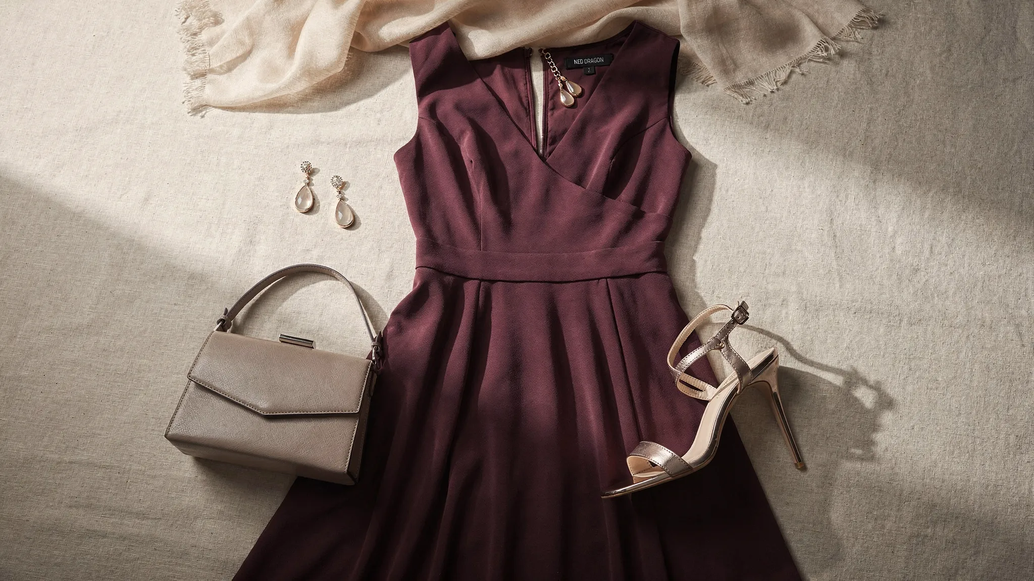 A complete cocktail party outfit laid out with a midi dress, strappy heels, a small clutch, delicate earrings, and a light wrap.