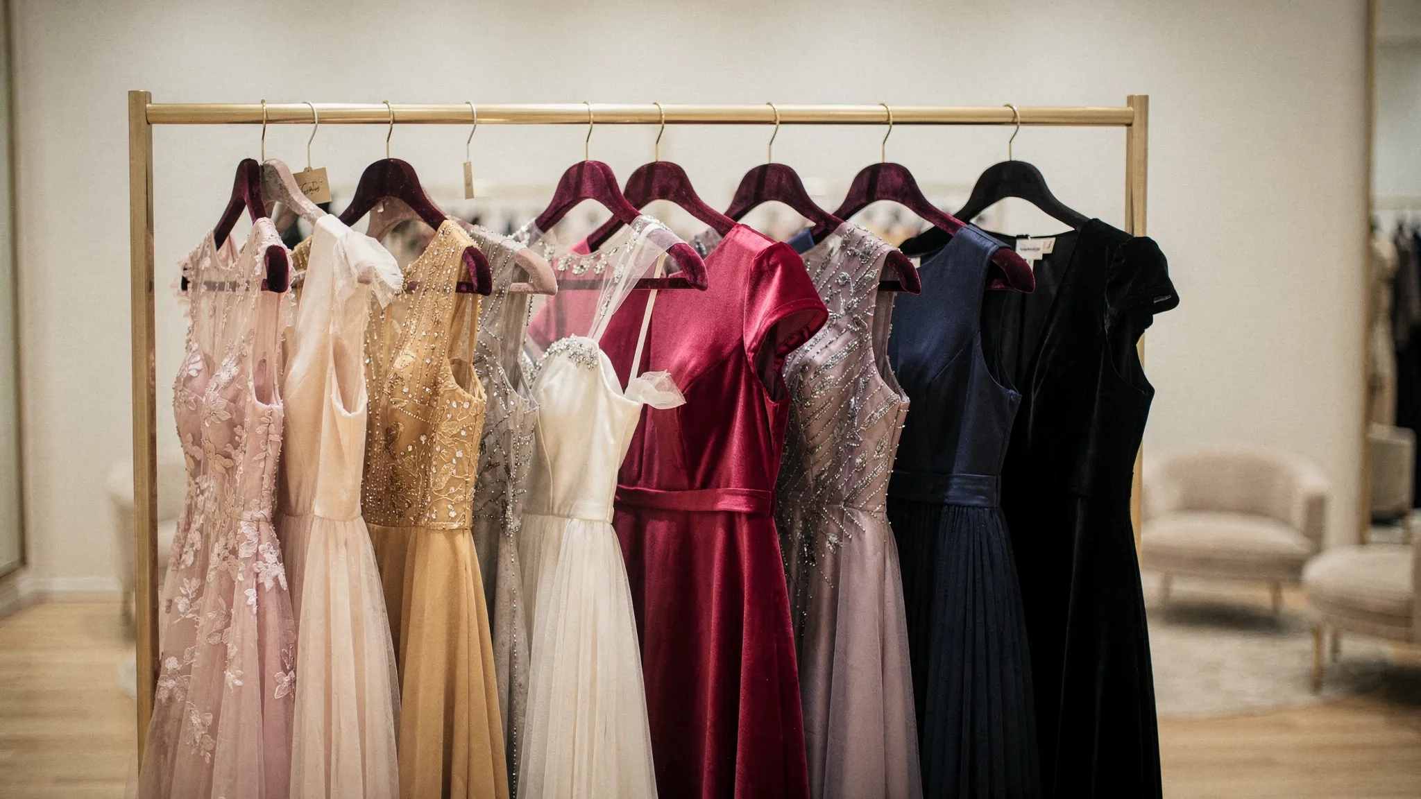 A curated rack of elegant cocktail dresses in satin, lace, chiffon, and crepe, arranged by color for weddings and evening parties.
